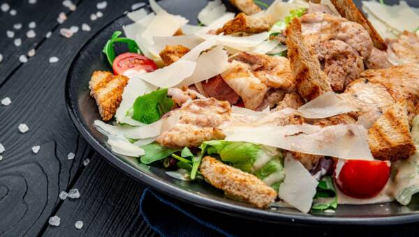 Świeża sałatka Cezar w białym talerzu na ciemnym drewnianym stole