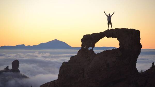 Mężczyzna z podniesioną ręką stojący na klifie - symbol motywacji