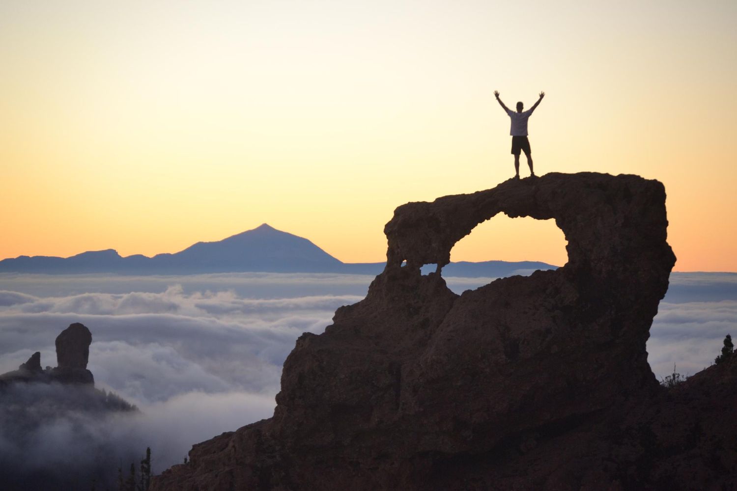 Mężczyzna z podniesioną ręką stojący na klifie  - symbol motywacji