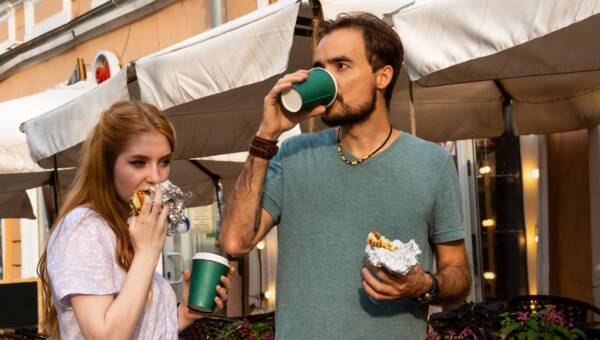 Młoda para jedząca jedzenie na wynos i pijąca kawę w pobliżu kawiarni