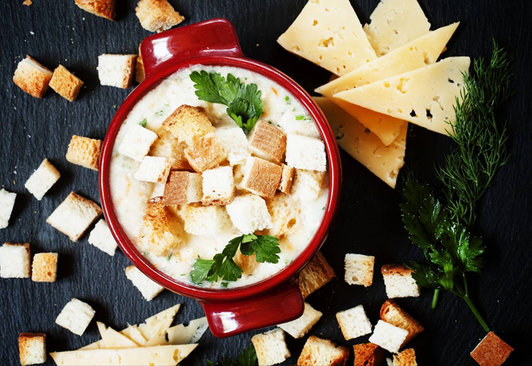 Cheese soup with croutons in red portioned saucepan, top view