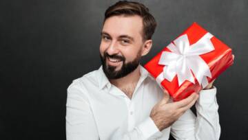 Portret ciekawskiego mężczyzny potrząsającego zapakowanym czerwonym pudełkiem i próbującego rozpoznać, co jest w środku