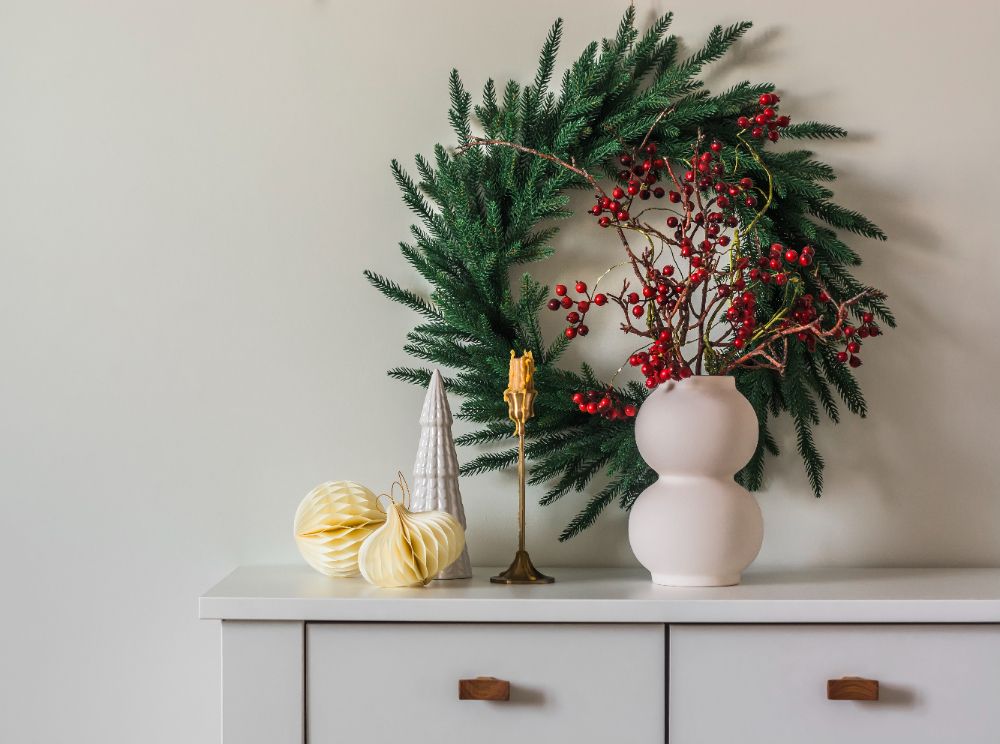 Wieniec świąteczny na ścianie wazon z gałęziami żurawiny świeca świąteczna dekoracja na białej szafce