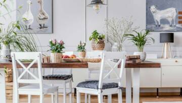 Białe krzesła przy drewnianym stole z kwiatami we wnętrzu jadalni z plakatami i lampą