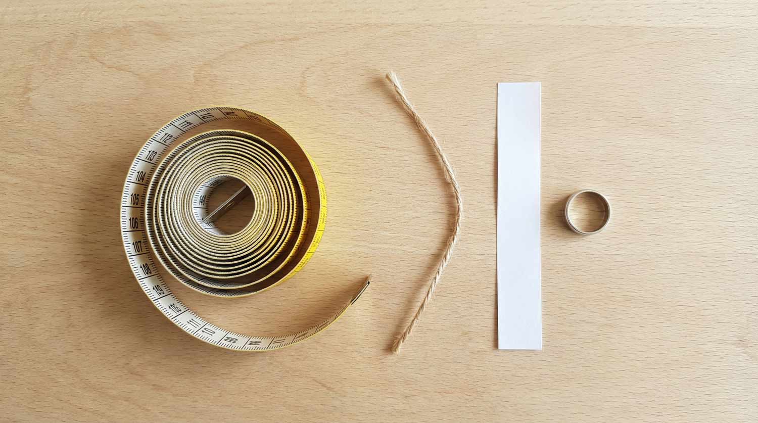 Różne narzędzia do mierzenia rozmiaru palca - miarka krawiecka, sznurek, papierowy pasek rozłożone na jasnym tle