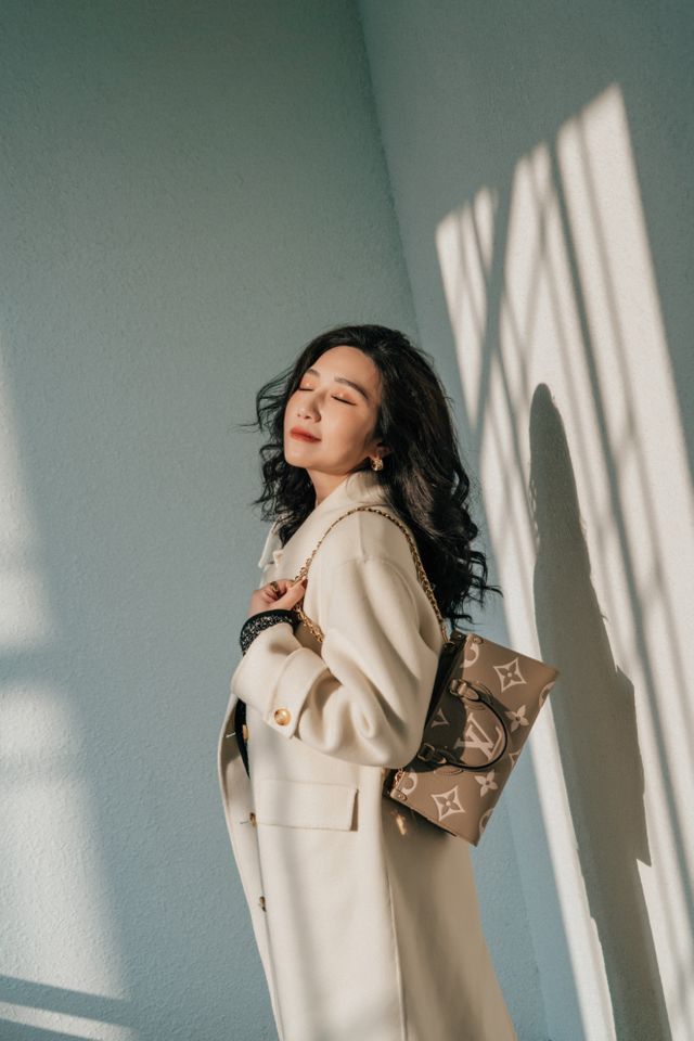Duża torebka Louis Vuitton z monogramem noszona na ramieniu do jasnego płaszcza