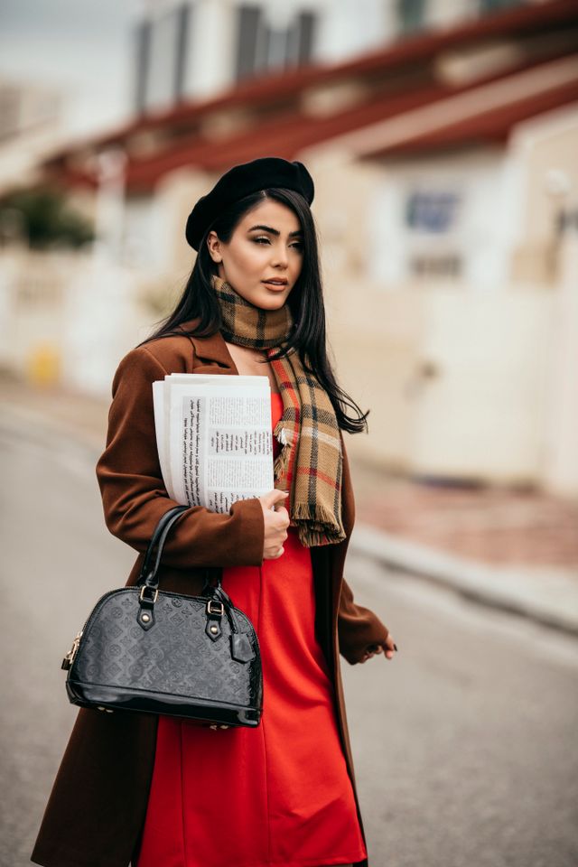 Czarna lakierowana torebka z tłoczonym monogramem w eleganckiej stylizacji street style z brązowym płaszczem, czerwoną sukienką i beretem