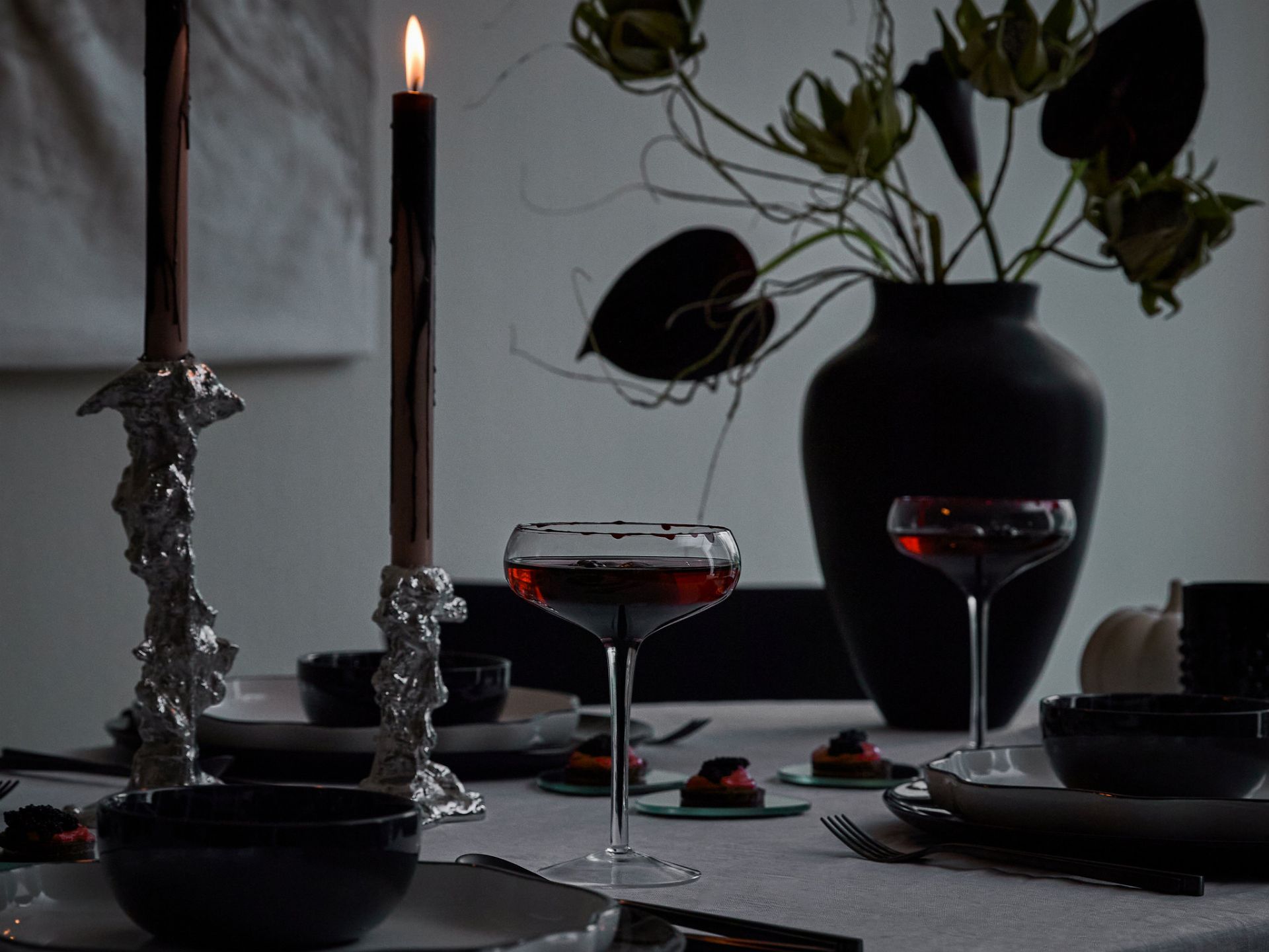 Eleganckie przyjęcie na Halloween: stół z czarnymi świecami, srebrzystymi świecznikami i kieliszkami z czerwonym napojem